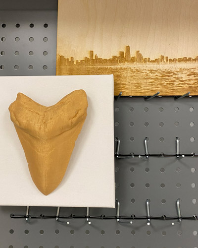 3D print of a giant shark tooth and an image of the Chicago skyline on a piece of wood, created with a laser cutter