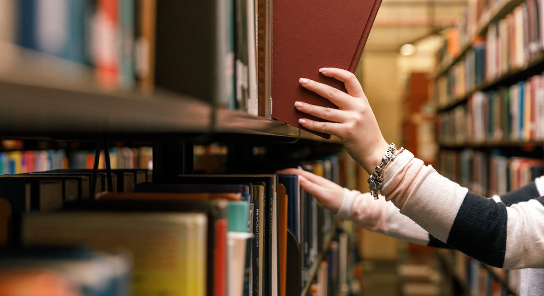 Close-up of someone removing a book from a shelf in the library
