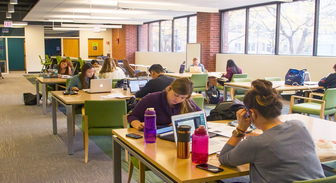 Students studying and working with laptops at tables in the Library of the Health Sciences.