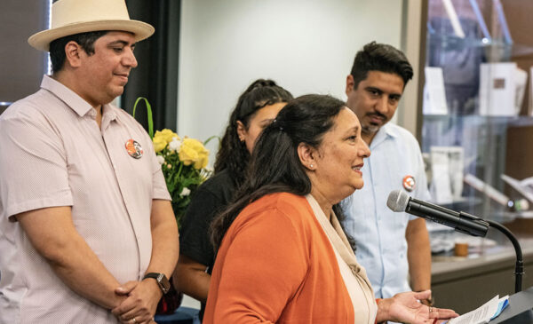 Profile view of Lupe Lozano speaking into a microphone at a podium surrounded by her two sons and granddaughter in the Circle Reading Room.