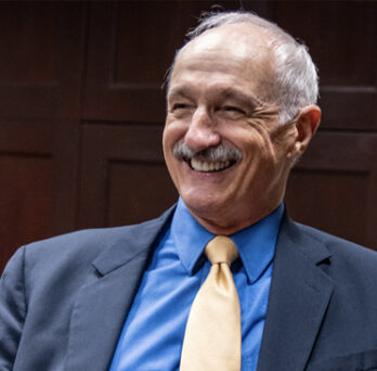 Actor Michael Gross smiling wearing blue jacket, blue shirt and gold tie. 