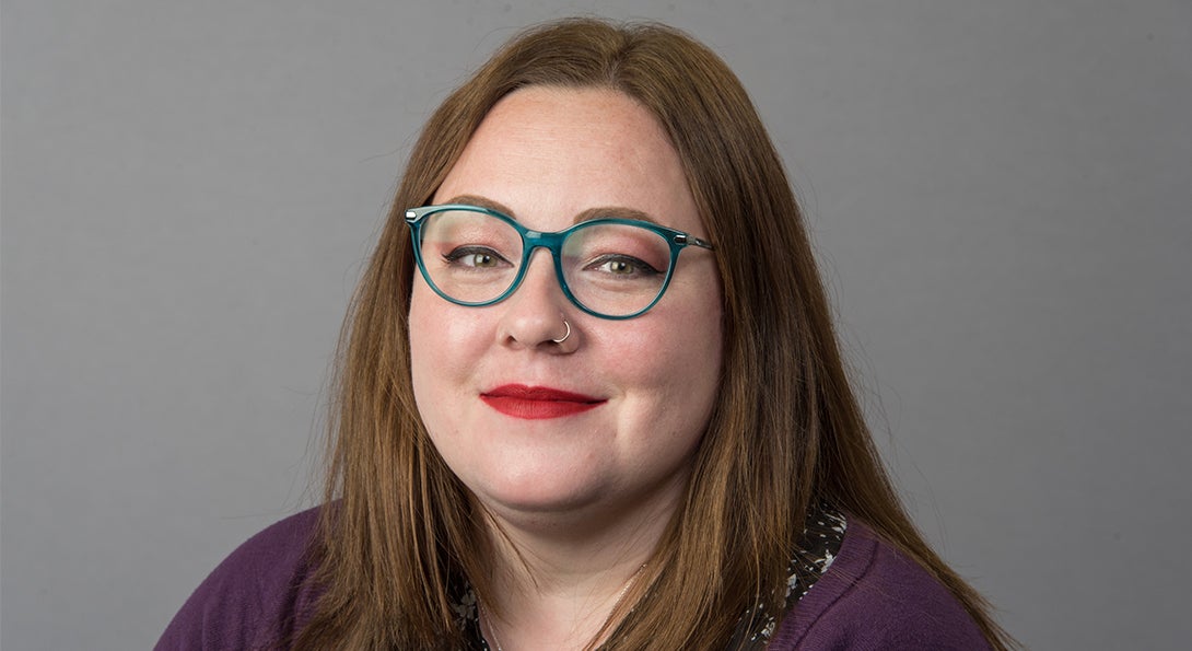 Emily Gilbert wearing teal glasses and a purple sweater on a neutral background.