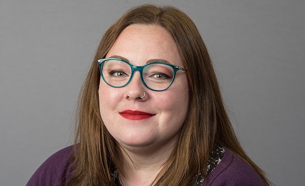 Emily Gilbert wearing teal glasses and a purple sweater on a neutral background.